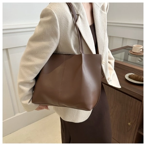 Brown leather tote bag featuring vertical stitching and long shoulder strap on model