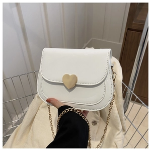 Detail of white patent leather saddle bag with golden heart lock and chain strap