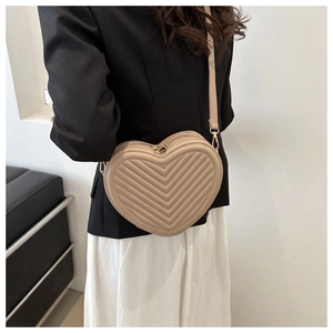 Detail of heart-shaped beige bag featuring V-shaped quilting and golden metal zippers