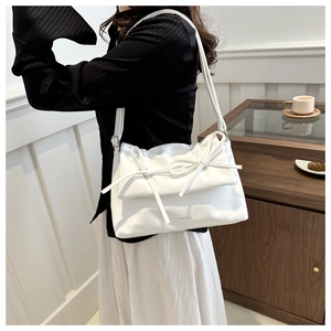 Detail of white pleated shoulder bag featuring a decorative bow and metallic logo print