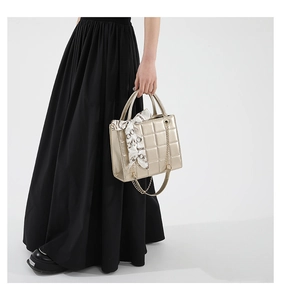 Close-up of quilted gold tote bag with decorative silk scarf and chain detailing