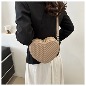 Detailed view of beige heart-shaped crossbody bag with V-quilted texture and gold zipper