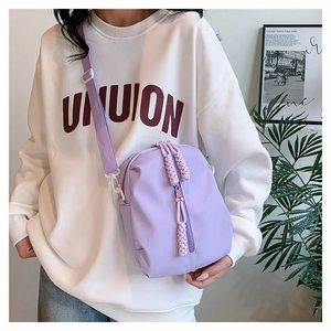 Detail of purple crossbody bag featuring round silhouette and woven rope zipper pull