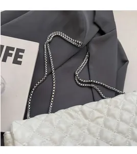 Detail of silver chain strap on white quilted crossbody bag with leather texture