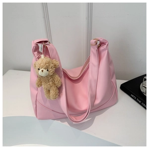 Detailed view of pink hobo shoulder bag with a cute brown plush bear charm on white desk