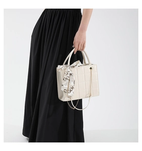 Close-up of cream quilted tote bag with golden chain and decorative silk scarf
