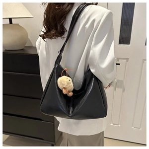 Minimalist black PU leather tote bag with yellow plush charm shown in a lifestyle setting