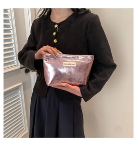 Detail of rose gold metallic handbag with woven 'FASHION BAG' label and zipper closure