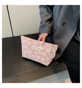 Detail of pink heart-embossed pouch with pearl zipper handle held by hand