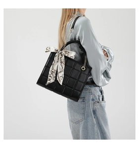 Close-up of black quilted tote bag with decorative silk scarf on the handle and gold hardware