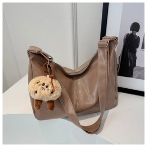 Detail of a large brown faux leather hobo tote bag featuring a cute plush pendant charm
