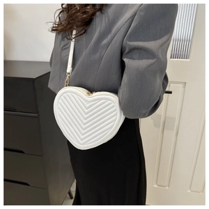 Detail of white heart-shaped crossbody bag with V-quilted texture and gold hardware