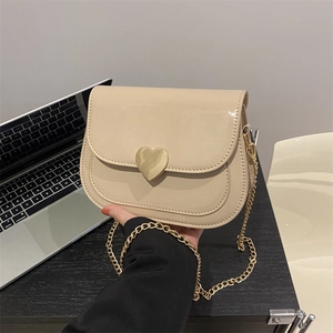 Chic beige crossbody saddle bag with gold heart buckle and chain strap on a desk