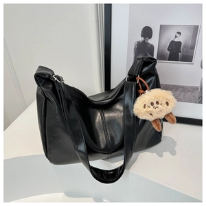 Detail of minimalist black leather tote bag with a khaki plush bear charm attachment