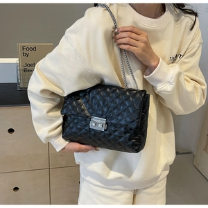 Close-up of black quilted shoulder bag with silver chain strap and metallic twist lock