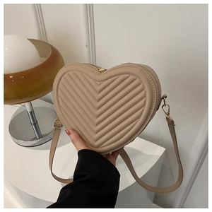 Close-up of beige heart-shaped bag featuring V-shaped quilting and gold metal zipper