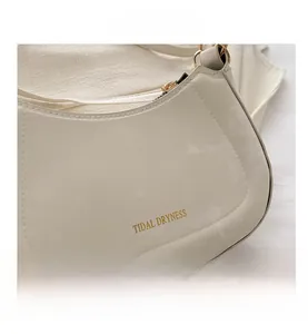 Detail shot of beige crescent bag featuring Tidal Dryness logo and gold zipper texture