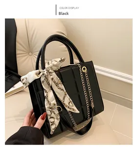 Detail of black quilted handbag with gold chain strap and elegant printed silk scarf handle