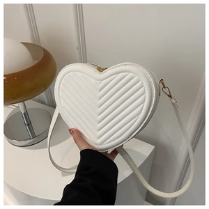 Detailed view of white heart-shaped crossbody bag with quilted V-pattern and gold hardware