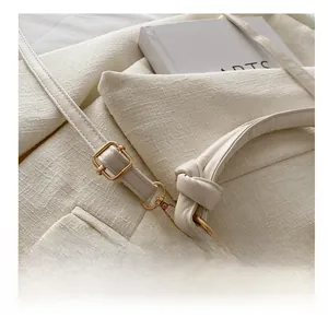 Detail of warm white leather bag showing champagne gold metal buckle and knotted strap