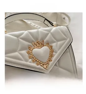 Detail of white quilted leather bag with ornate golden crown heart buckle and texture