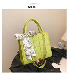 Detail of green square handbag with quilted texture, gold chain and decorative silk scarf