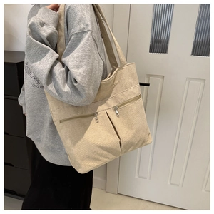 Detail view of beige corduroy tote bag with dual front zipper pockets on model shoulder