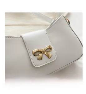 Close-up of white leather crescent bag with detailed gold metal bow buckle decoration