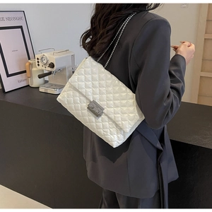 White quilted crossbody bag with silver chain strap worn by a model in a grey blazer