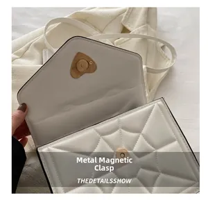 Macro detail of the golden heart-shaped magnetic clasp on white quilted leather bag