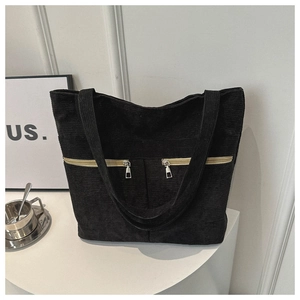 Detail of black corduroy tote bag showing dual zipper front pockets and textured fabric