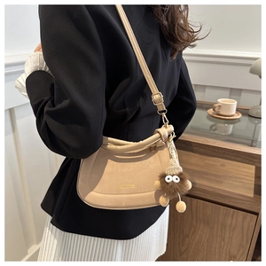 Close-up of beige suede semi-circular shoulder bag with cute plush eye pendant