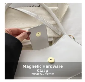 Close-up of golden magnetic hardware buckle on white leather minimalist shoulder bag