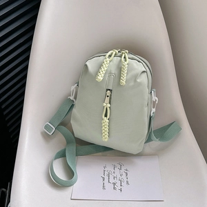 Minimalist mint green nylon crossbody bag with woven zipper pulls on a modern chair