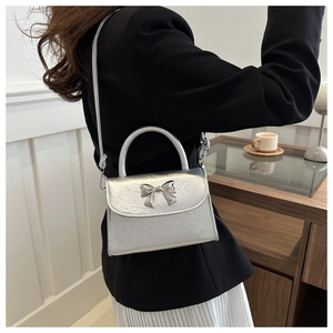 Detail of silver crossbody bag with metallic bow ornament and textured leather