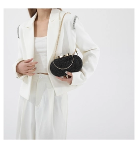 Detail of black glitter evening clutch with bow clasp and gold chain on white suit