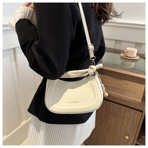 Detail of white half-moon leather crossbody bag with knot handle and plush charm