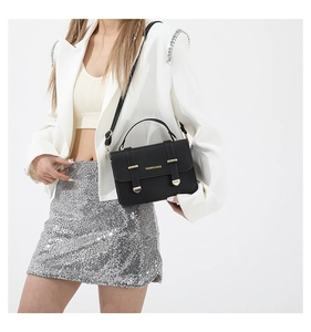 Detail of black crossbody bag with gold clasp and textured strap on a white blazer