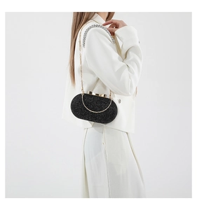 Detail of black sequin evening bag with gold handle and metal chain on white suit background