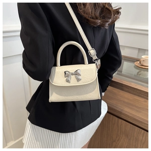 Close-up of cream white crossbody bag featuring a silver metal bow and lychee texture