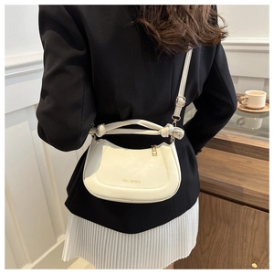 Detail of a beige half-moon bag featuring a unique knotted handle and lychee leather texture