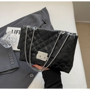 Detail of black quilted shoulder bag with silver square lock and metallic chain strap