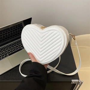 White heart-shaped crossbody bag with V-quilting and adjustable strap in a casual setting