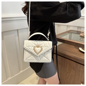 Detail of white quilted crossbody bag featuring a golden crown-heart shaped clasp