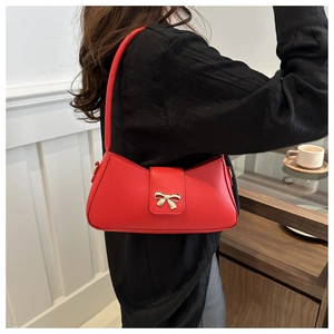 Détail d'un sac sous le bras en cuir rouge avec un fermoir nœud doré sur fond lifestyle
