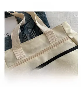 Detail view of large canvas tote bag with metal zipper closure and black stripe accent
