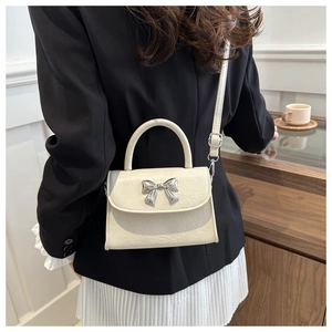 Detail of cream white leather handbag with silver metal bow on a model shoulder