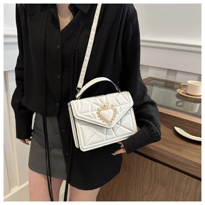 Detail of white quilted crossbody bag with golden heart crown clasp on elegant outfit
