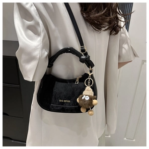 Detail of black crescent shoulder bag with gold logo and brown plush monster charm