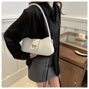 Détail d'un sac baguette blanc en similicuir avec un fermoir nœud en métal doré sur le rabat